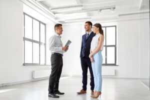 real estate business, sale and people concept - happy smiling realtor with folder and customers at new office room
